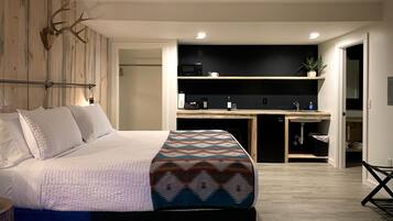 Un dormitorio moderno con una cama grande, una pared de madera con una cabeza de animal montada, y una zona de cocina con microondas, lavamanos y estanterías.