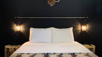 A bed with white linens, two bedside lamps, a wooden headboard, and a wall-mounted deer skull.