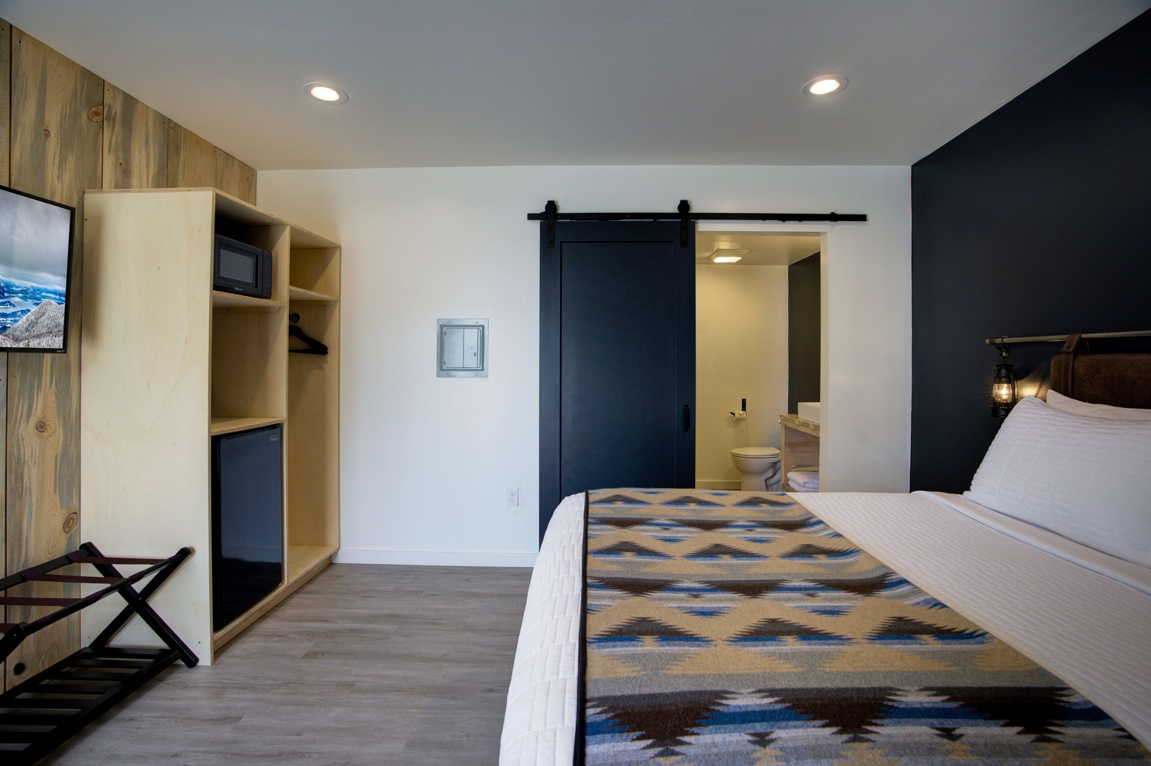 Quarto com cama, guarda-roupa de madeira, televisão e porta deslizante para um banheiro.
