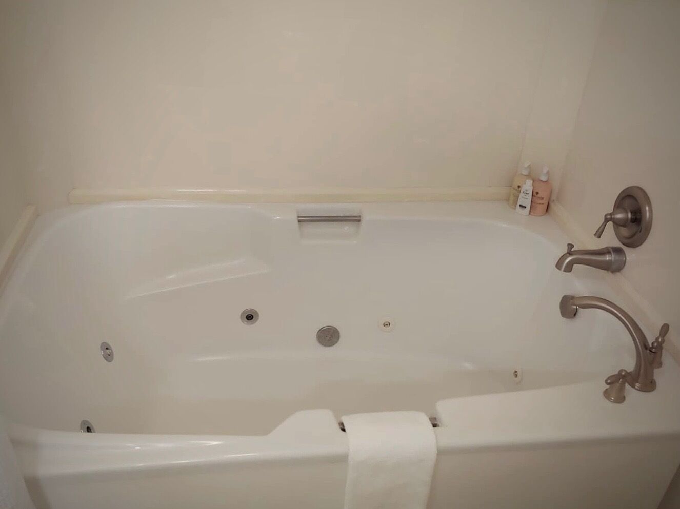 Una bañera blanca con un solo grifo y un cabezal de ducha de mano, una toalla colgada a un lado y un pequeño estante con artículos de aseo.