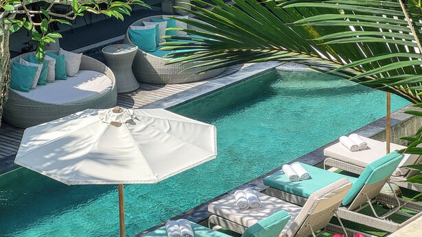 A poolside area with lounge chairs, a sun umbrella, and a small seating area with cushions. - The Palms Canggu (Canggu)