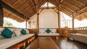 A room with a wooden floor, a sofa with teal pillows, a wooden coffee table, and a thatched roof. - The Palms Canggu (Canggu)