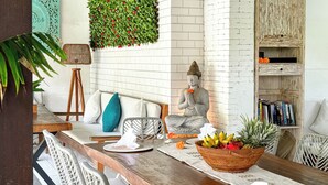 A dining area with a long wooden table, wicker chairs, a statue, a wall-mounted plant, and a bookshelf. - The Palms Canggu (Canggu)