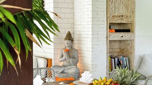 A statue of a seated figure, a wicker basket with fruits, and a white brick wall. - The Palms Canggu (Canggu)
