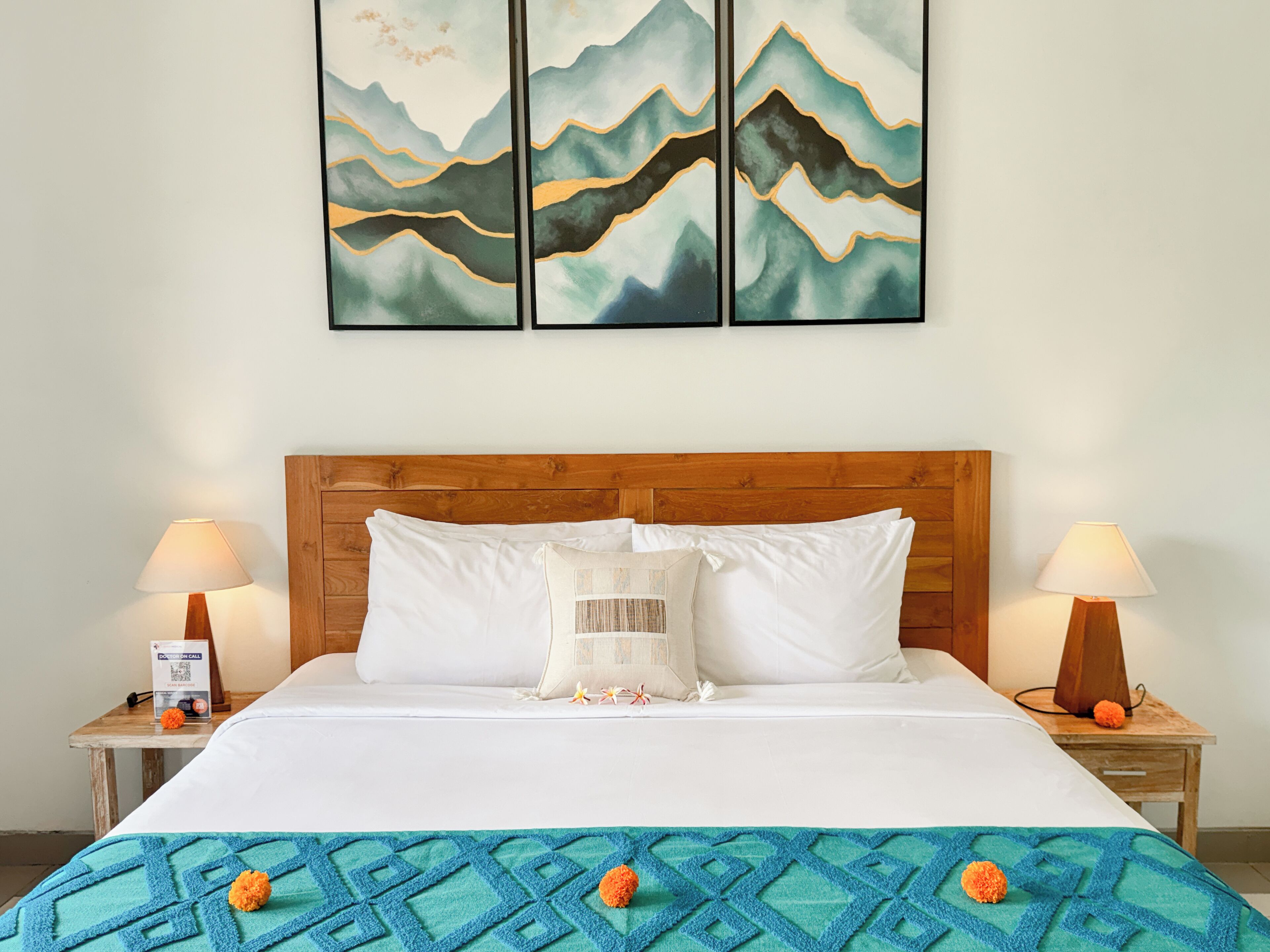 Una habitación de hotel con cabecera de madera, ropa de cama blanca, un plaid azul estampada y dos lámparas de noche.