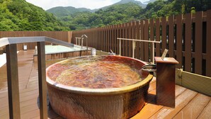 A hot tub on a wooden deck with a view of lush green mountains in the background. - Yugawara Chiyodasou (Yugawara)