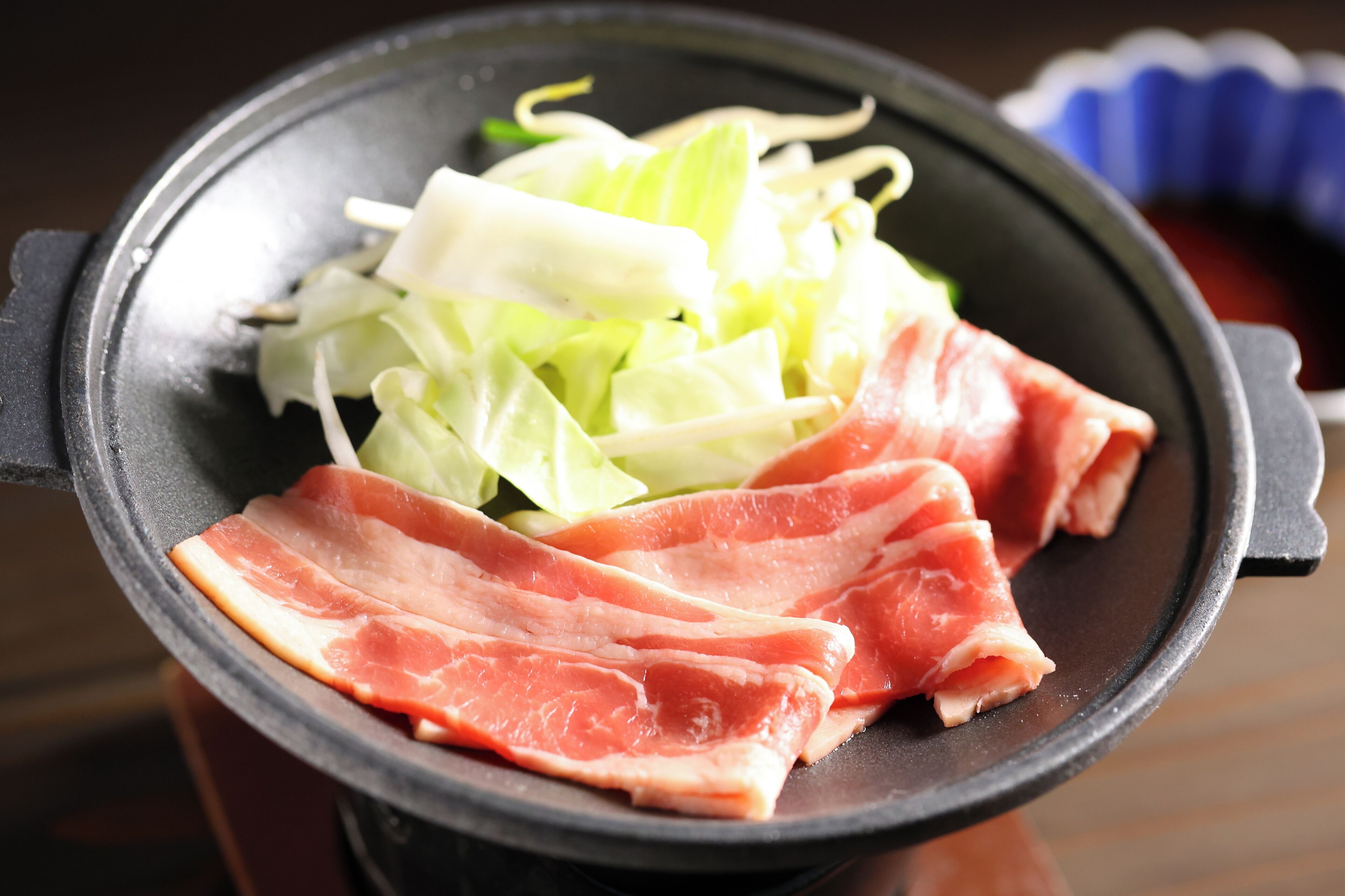 A hot pot with thinly sliced meat and leafy greens.