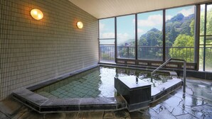 A hot tub with a view of a forested hillside through large windows. - Yugawara Chiyodasou (Yugawara)