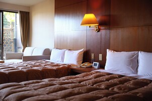 Habitación de hotel con dos camas, una mesita de noche con lámpara, teléfono y una silla.