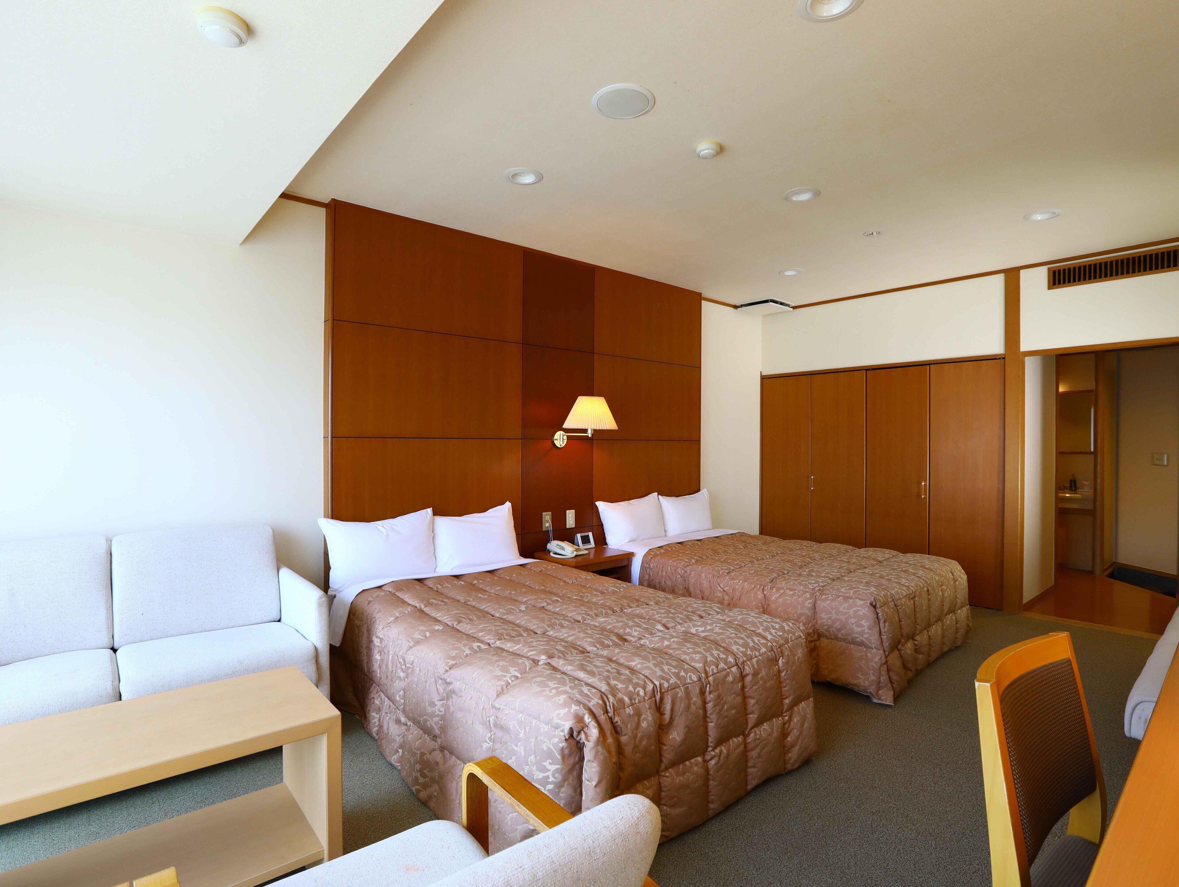 A hotel room with two beds, a sofa, a desk, and a wardrobe.