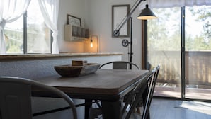 A dining area with a wooden table, chairs, a bowl of bread, and a pendant light.