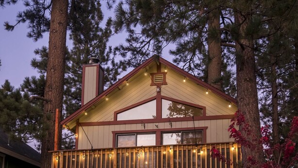 A two-story wooden cabin with a balcony, surrounded by trees.