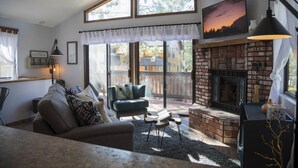 A cozy living room with a fireplace, a comfortable sofa, and a large window offering a view of the backyard.