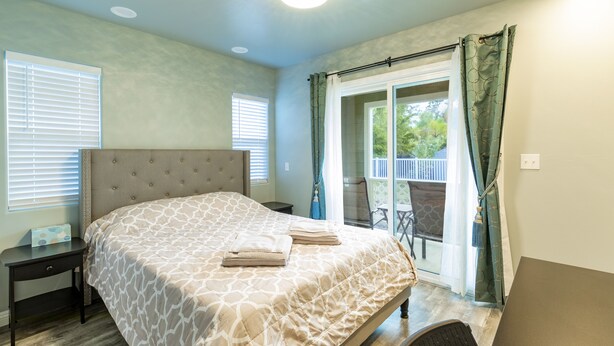 A bedroom with a large bed, a nightstand, a desk, and a sliding glass door to a balcony. - Ocean Breeze Inn 2 Bedroom, 3 Full Bathroom, 1 Kitchen Apartment (Keaau)