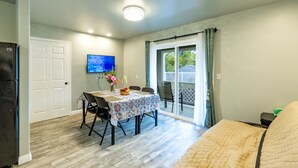 A compact living space with a dining area, a sofa, a TV, and a sliding glass door to a patio. - Ocean Breeze Inn 2 Bedroom, 3 Full Bathroom, 1 Kitchen Apartment (Keaau)