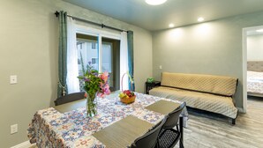 A small, well-lit room with a dining table set for two, a sofa, and a bed. - Ocean Breeze Inn 2 Bedroom, 3 Full Bathroom, 1 Kitchen Apartment (Keaau)