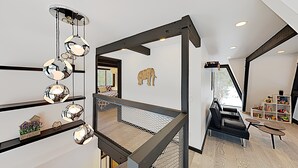 Un intérieur moderne avec un escalier, un canapé en cuir noir et une décoration murale représentant un éléphant en bois.