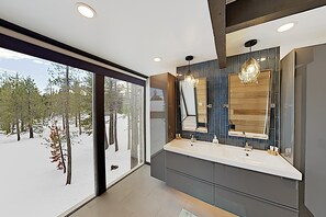 Une salle de bain moderne dotée d’une grande fenêtre, de deux vasques et d’un miroir agrémenté d’un panneau en bois en arrière-plan.
