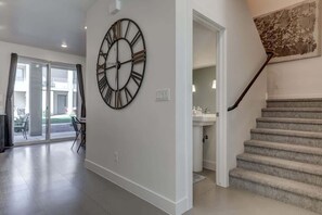 A modern interior with a large wall clock, a staircase, and a view through glass doors.