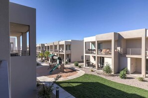 A modern residential building with multiple balconies, a playground, and a well-maintained lawn.