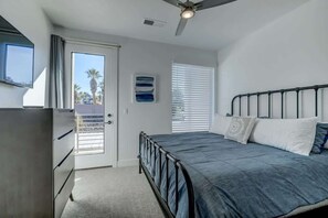 A bedroom with a bed, a ceiling fan, a window with blinds, and a door.