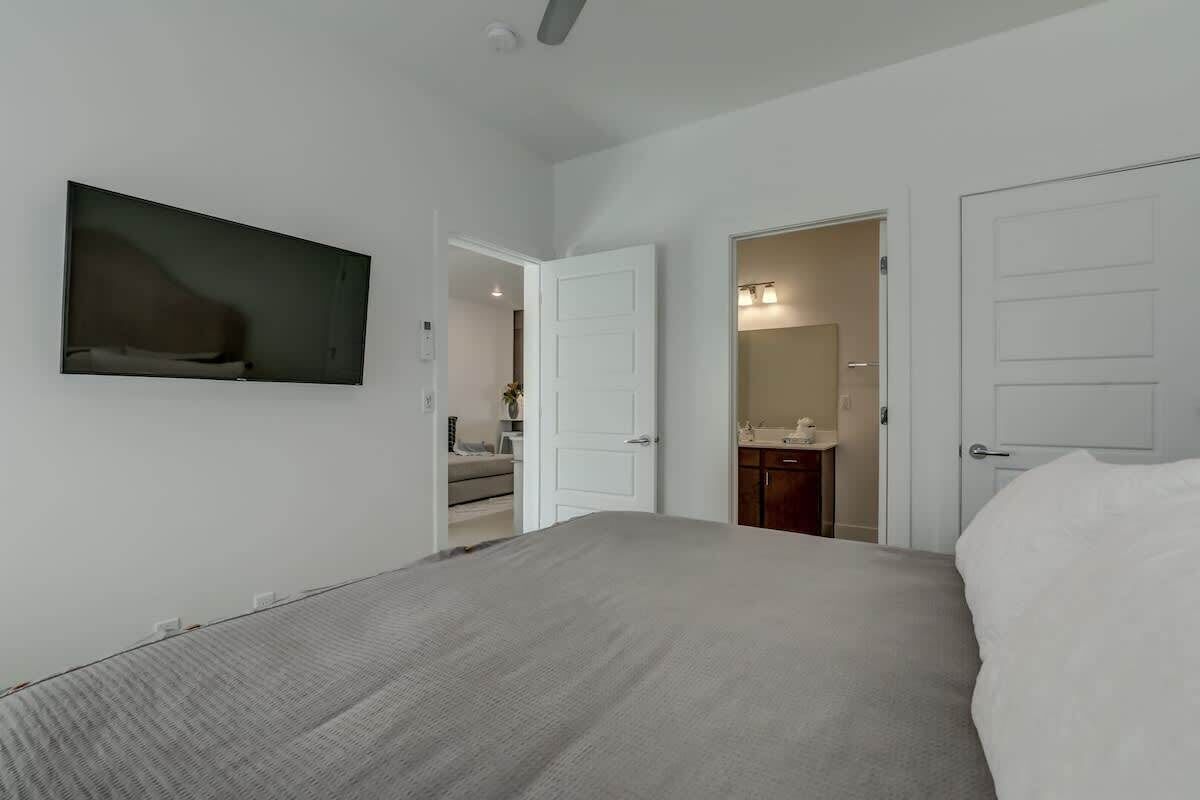 A bedroom with a bed, a door leading to a bathroom, and a wall-mounted TV.