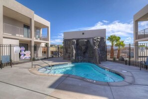A swimming pool with a rock feature, surrounded by a fence, and adjacent to a building with balconies.