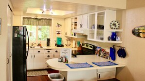 Una cocina compacta con armarios blancos, un refrigerador negro, una cafetera y una pequeña isla con un tapete.