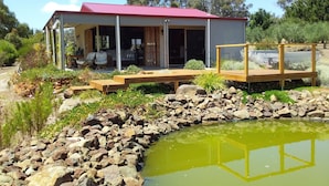 Une maison moderne dotée d’un porche abrité, d’une piscine et d’un jardin agrémenté de rochers et de plantes.