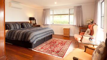 A bedroom with a large bed, a nightstand, a chair, a small table, and a window with curtains.