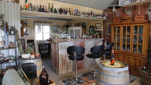Un coin bar au style rustique, avec des tabourets de bar en bois, un meuble en bois doté de portes en verre et diverses bouteilles exposées sur des étagères.