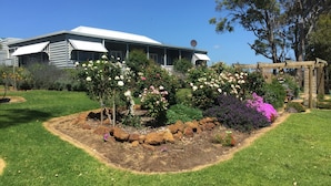 Une maison avec un jardin à l’avant, comprenant une pelouse, un jardin de rocaille et diverses plantes à fleurs.