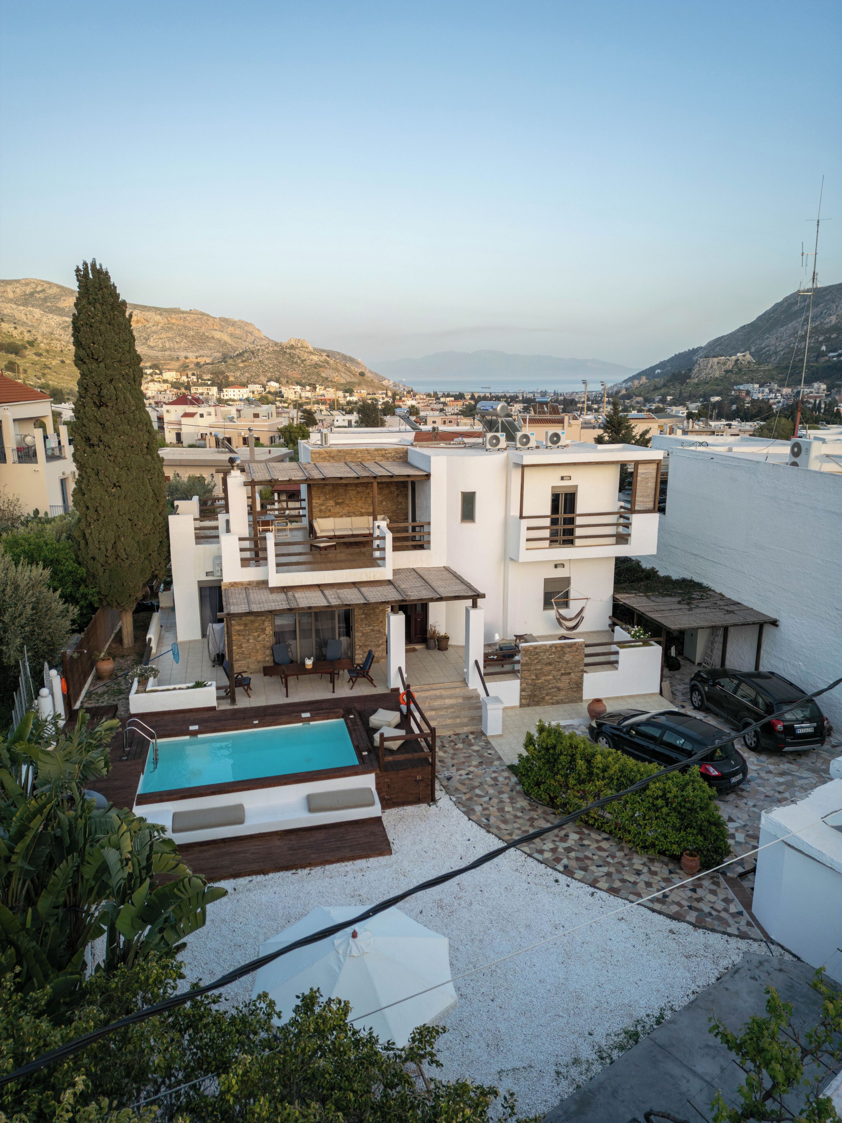 A modern two-story house with a swimming pool, outdoor seating, and a view of the sea.