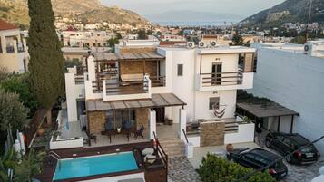 A modern two-story house with a swimming pool, outdoor seating, and a view of the sea.