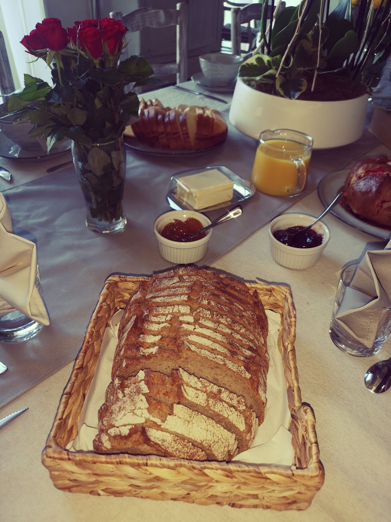 Une table mise pour le petit-déjeuner avec du pain, du beurre, de la confiture et un vase de roses.