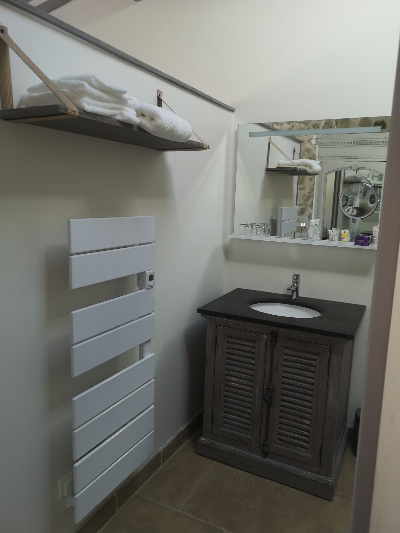 A bathroom with a white towel rack, a white cabinet with drawers, a black sink vanity, and a mirror with a decorative frame.