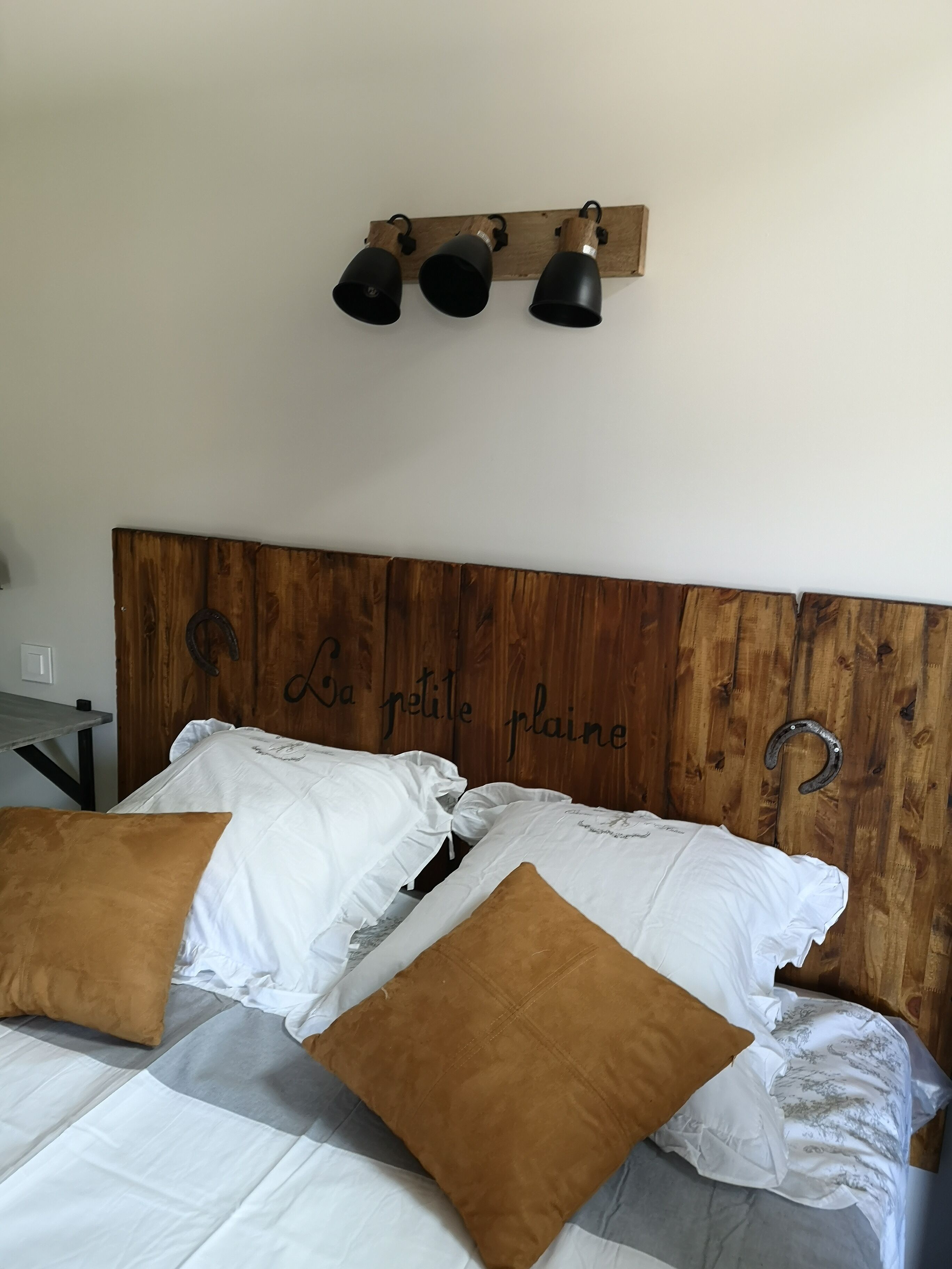 Een bed met een houten hoofdbord, witte en bruine kussens, en drie zwarte wandlampen.