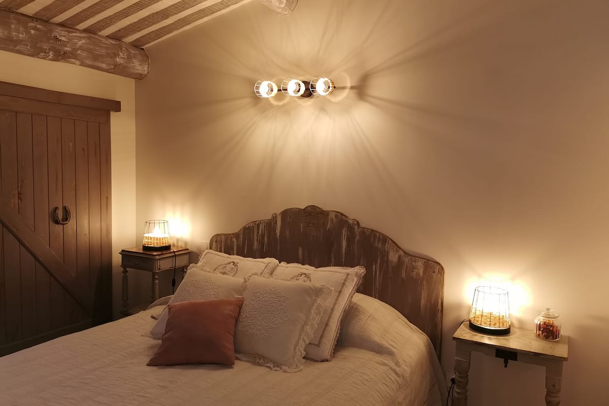 Un dormitorio con cabecera de madera, cama con almohadas estampadas y dos mesitas de noche con lámparas.