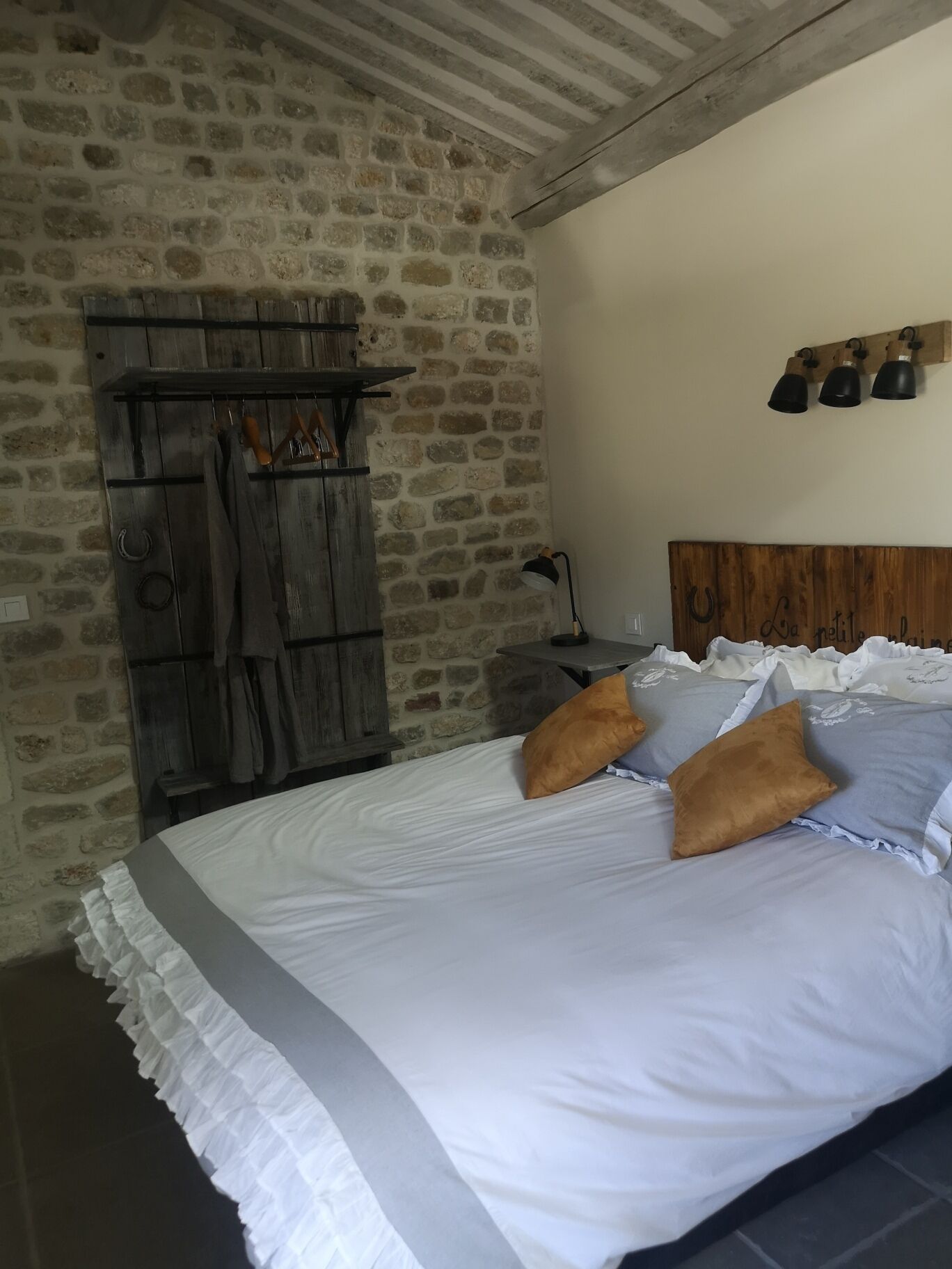 Un dormitorio con pared de piedra, cabecero de madera y cama con ropa de cama blanca y dos almohadas.