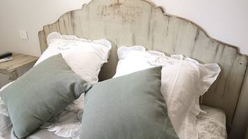 Un letto con cuscini bianchi e verdi, una testiera in legno e un piccolo comodino con un telecomando.