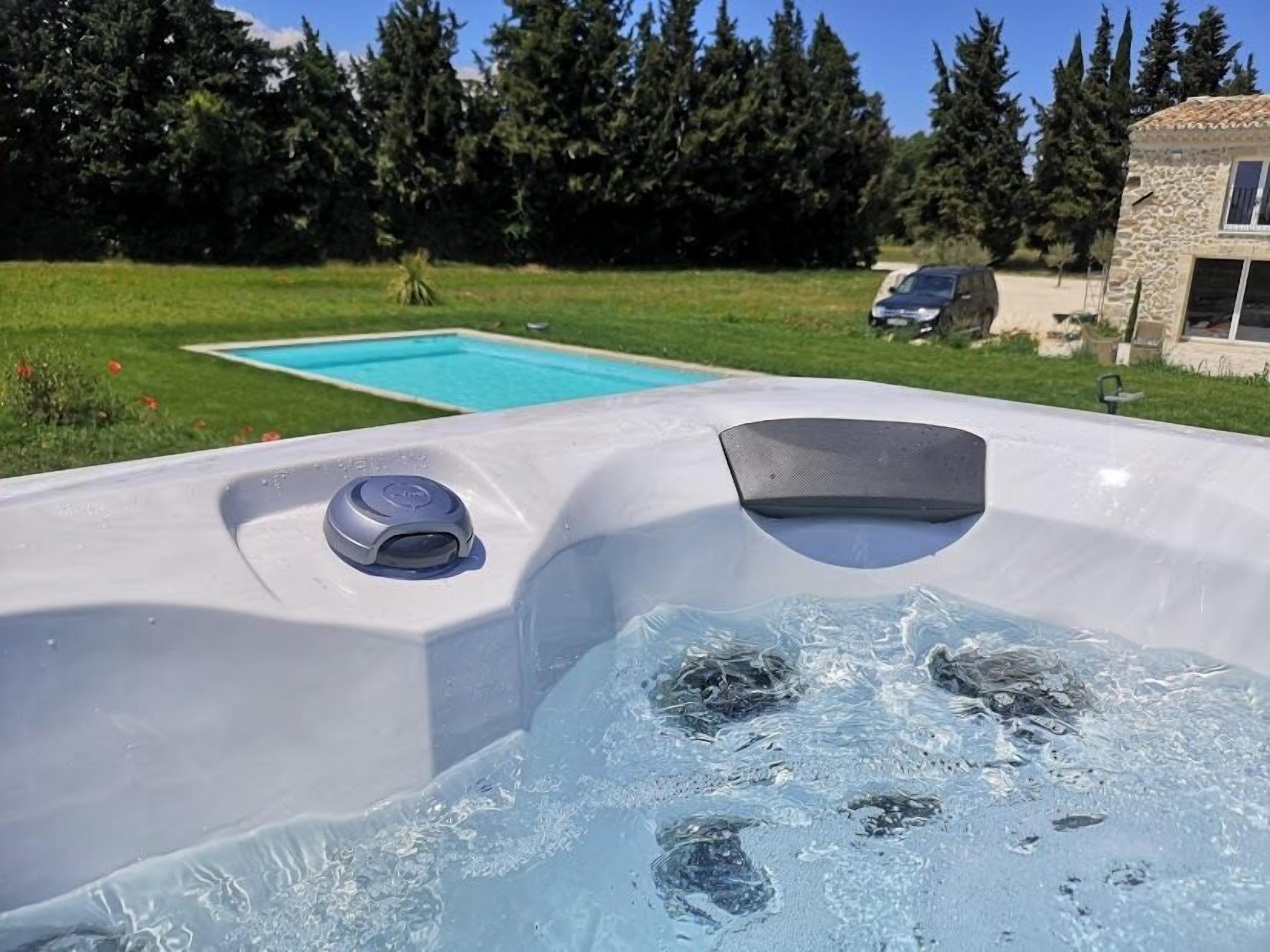 A hot tub with a control panel and a view of a swimming pool and greenery in the background.