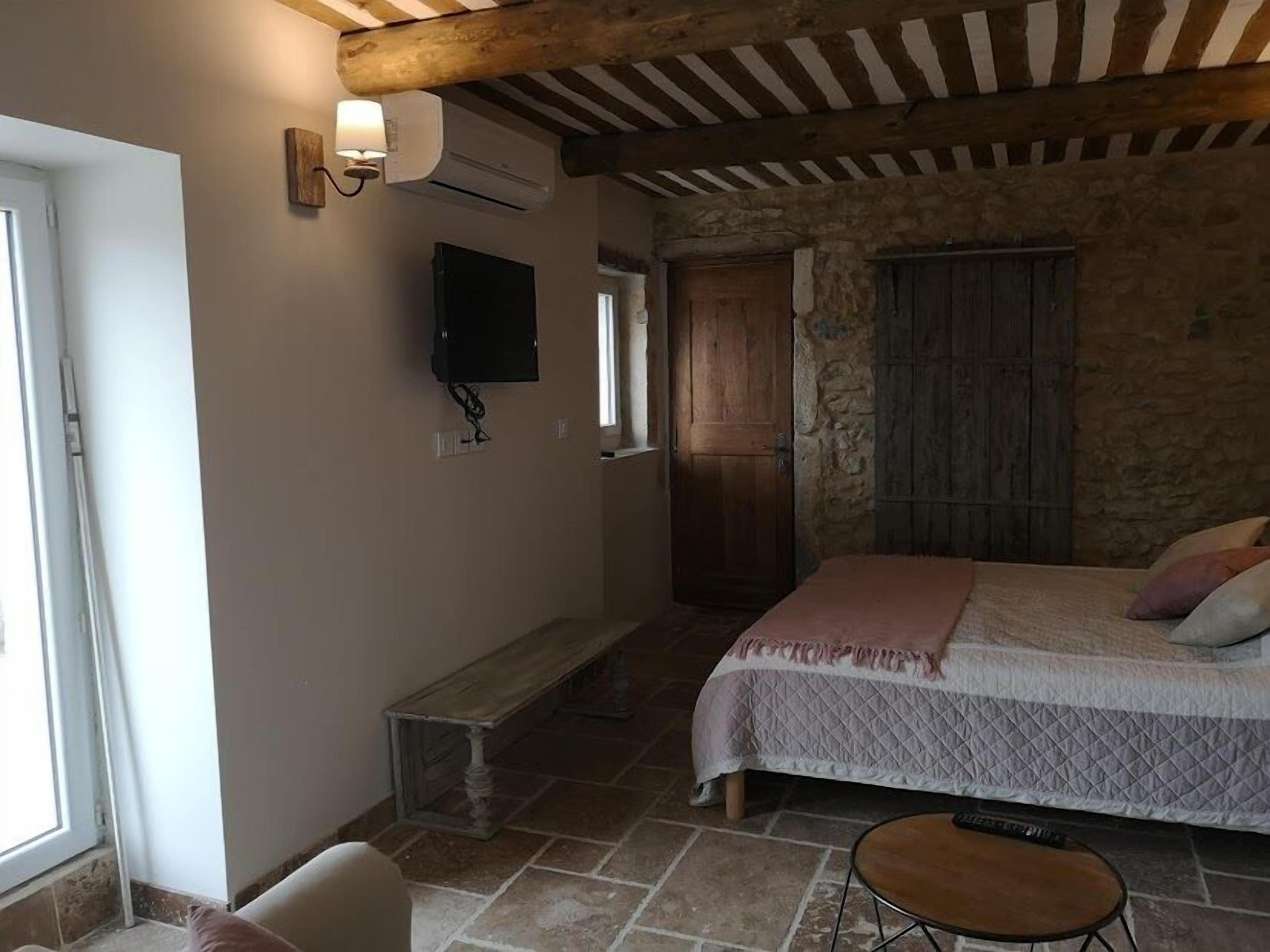 Un dormitorio con cama, una banca, un televisor y una pared de piedra.