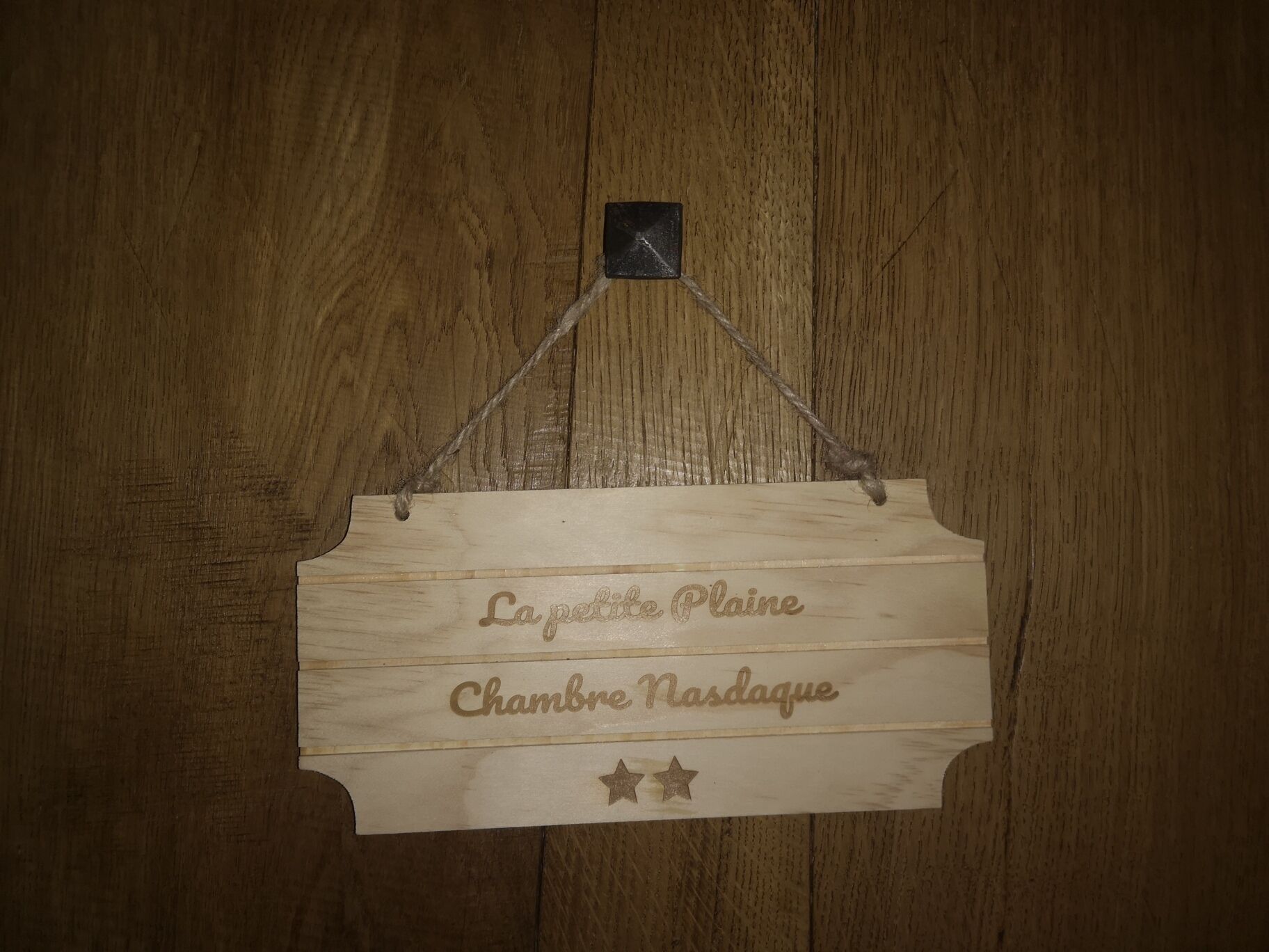 A wooden sign with the text "La petite Plaine Chambre Nasdale" and two stars below it.