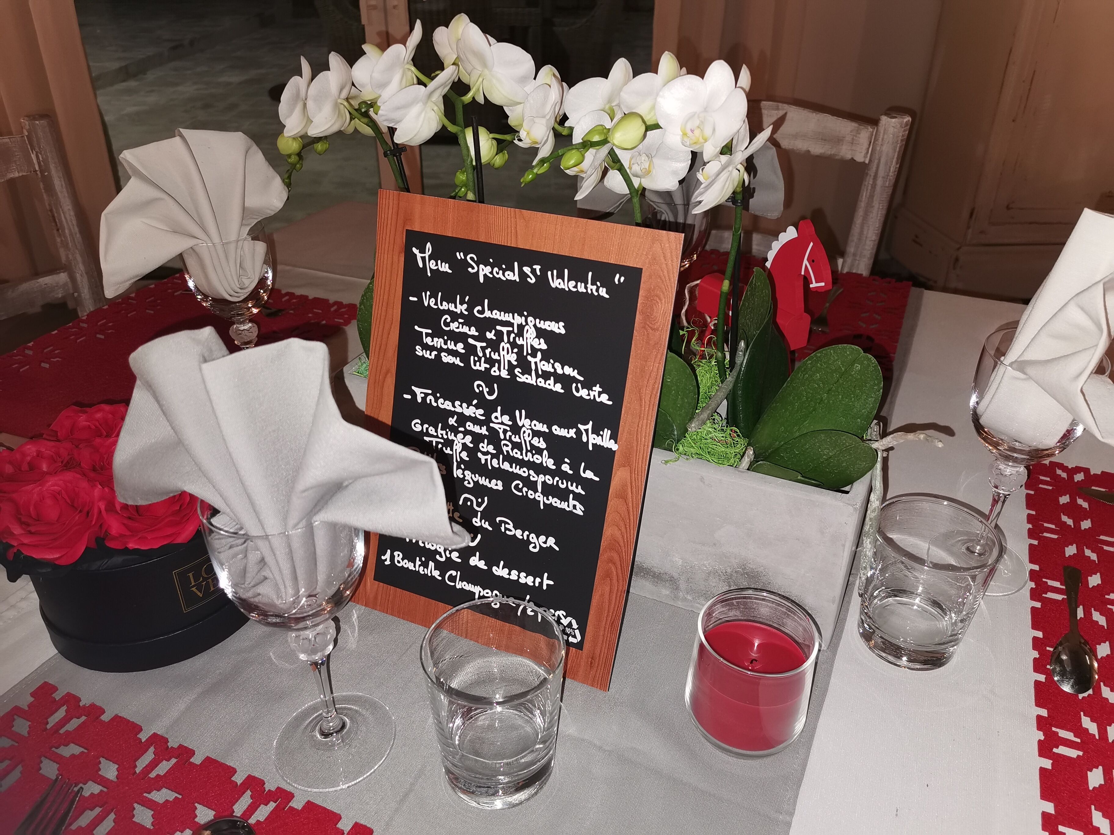 A table set with a menu, white flowers, red roses, and a candle.