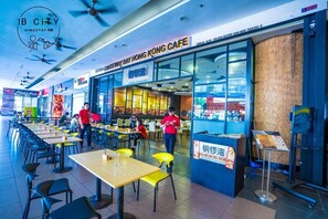 Un restaurante moderno con fachada de vidrio, mesas al aire libre y un letrero azul.