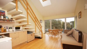 Una cocina moderna con armarios de madera, un comedor con mesa y sillas, y un sofá en una sala de estar luminosa con ventanas amplias.