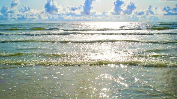 Una playa con cielos despejados y el sol reflejándose en el agua.