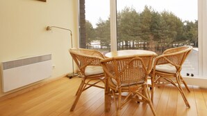 Una habitación con un ventanal grande, sillas de mimbre, una mesa y un radiador.