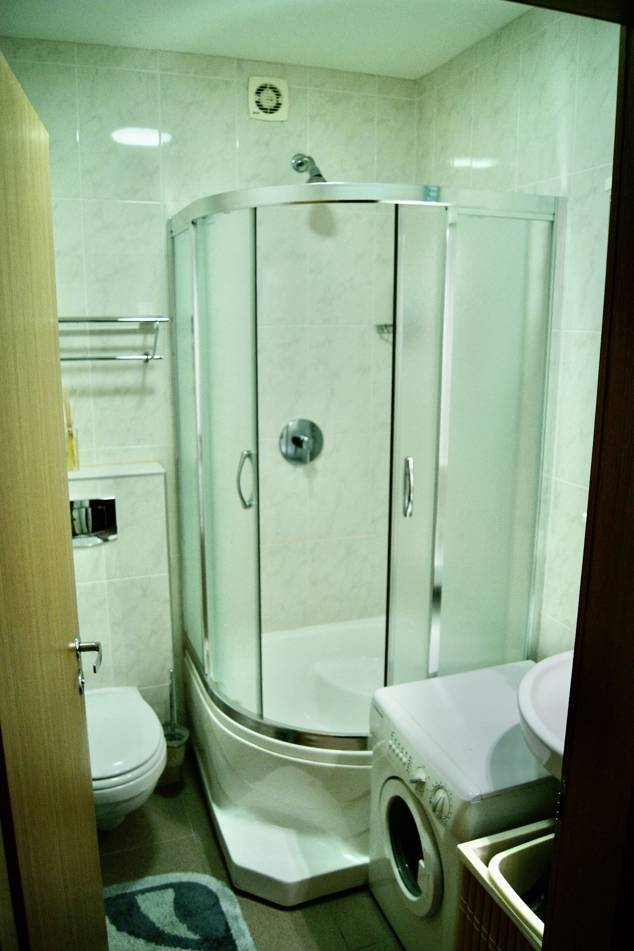 Een kleine badkamer met douchecabine, toilet en wasmachine.