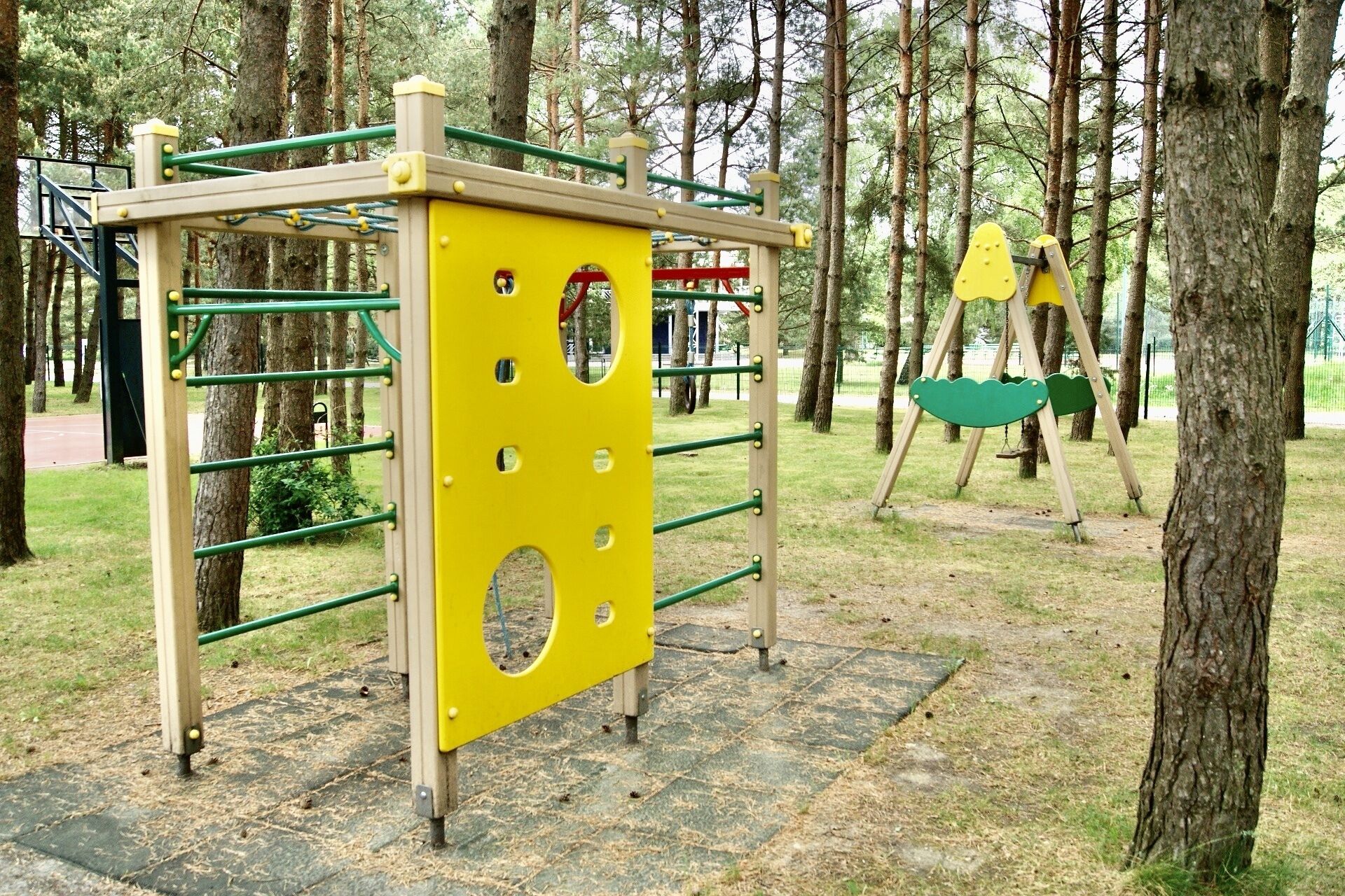 Un parque infantil con una estructura amarilla para escalar y columpios.